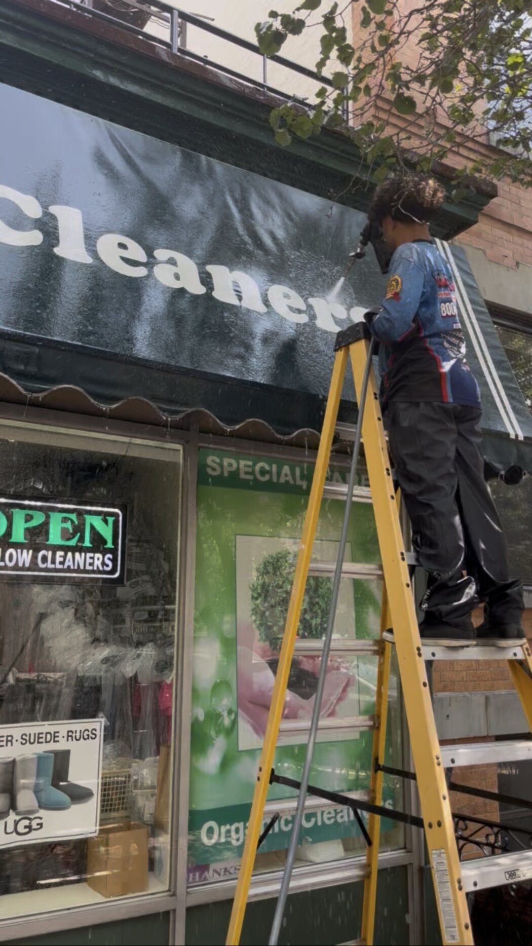 Crew rinsing a fabric storefront awning from a ladder