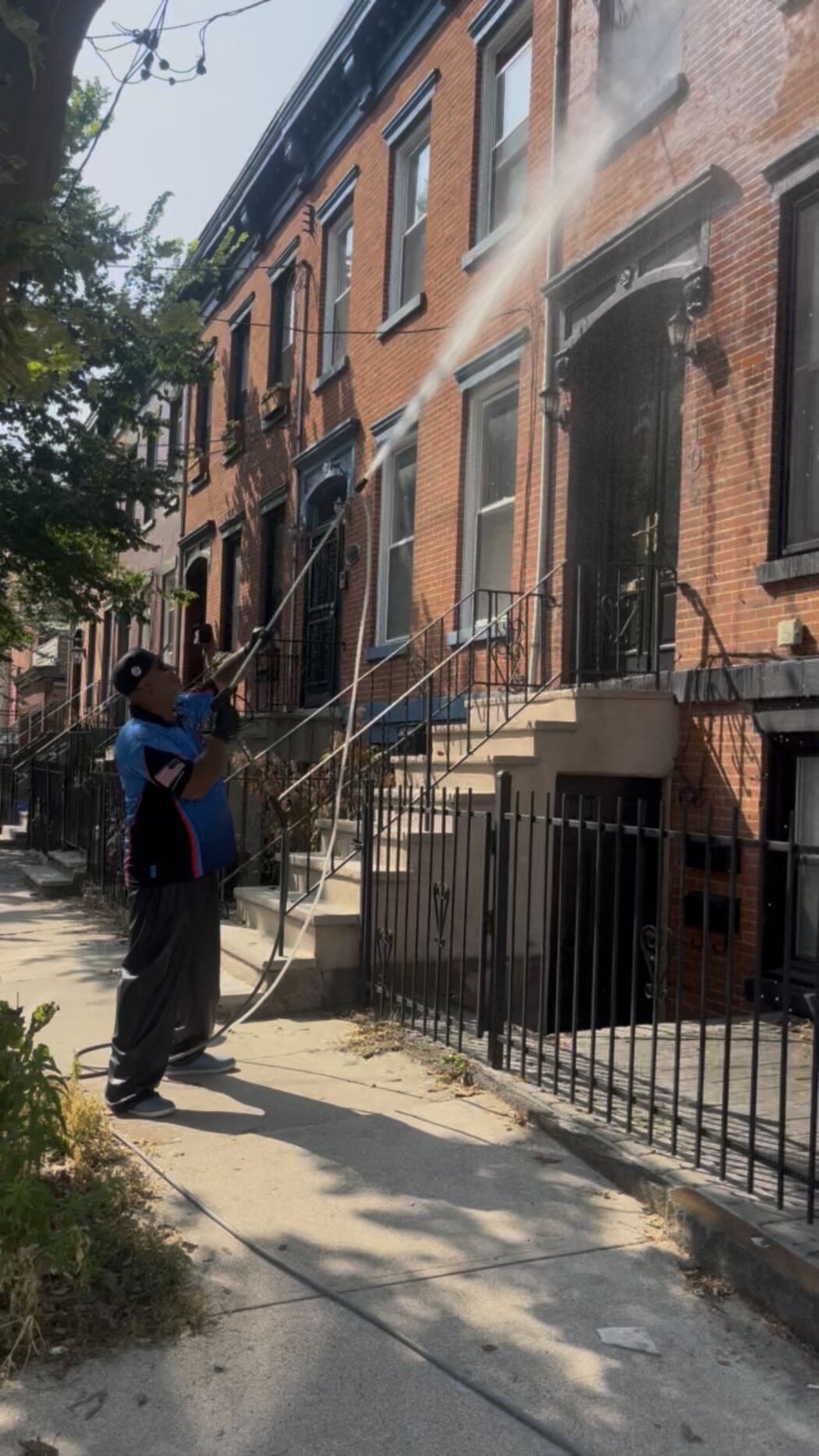 Crew washing a brick rowhouse facade with a telescopic wand