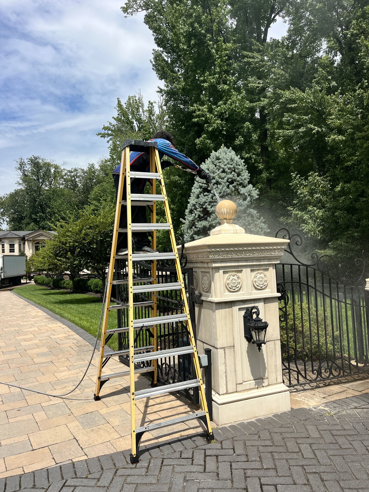 Crew member on a ladder soft washing a carved stone entrance pillar at an estate gate