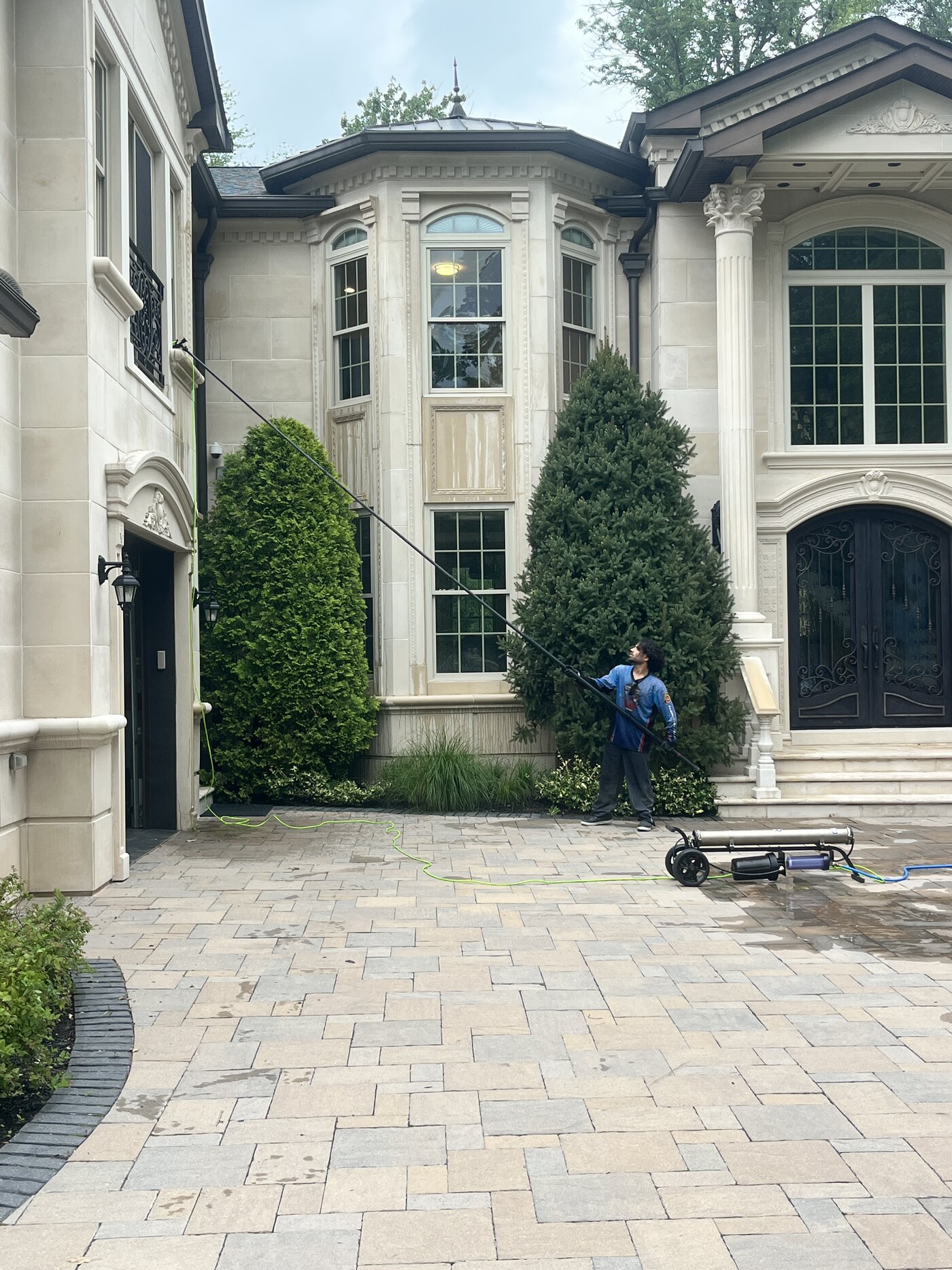 Crew soft washing streaked cast limestone on an estate courtyard with a water fed pole