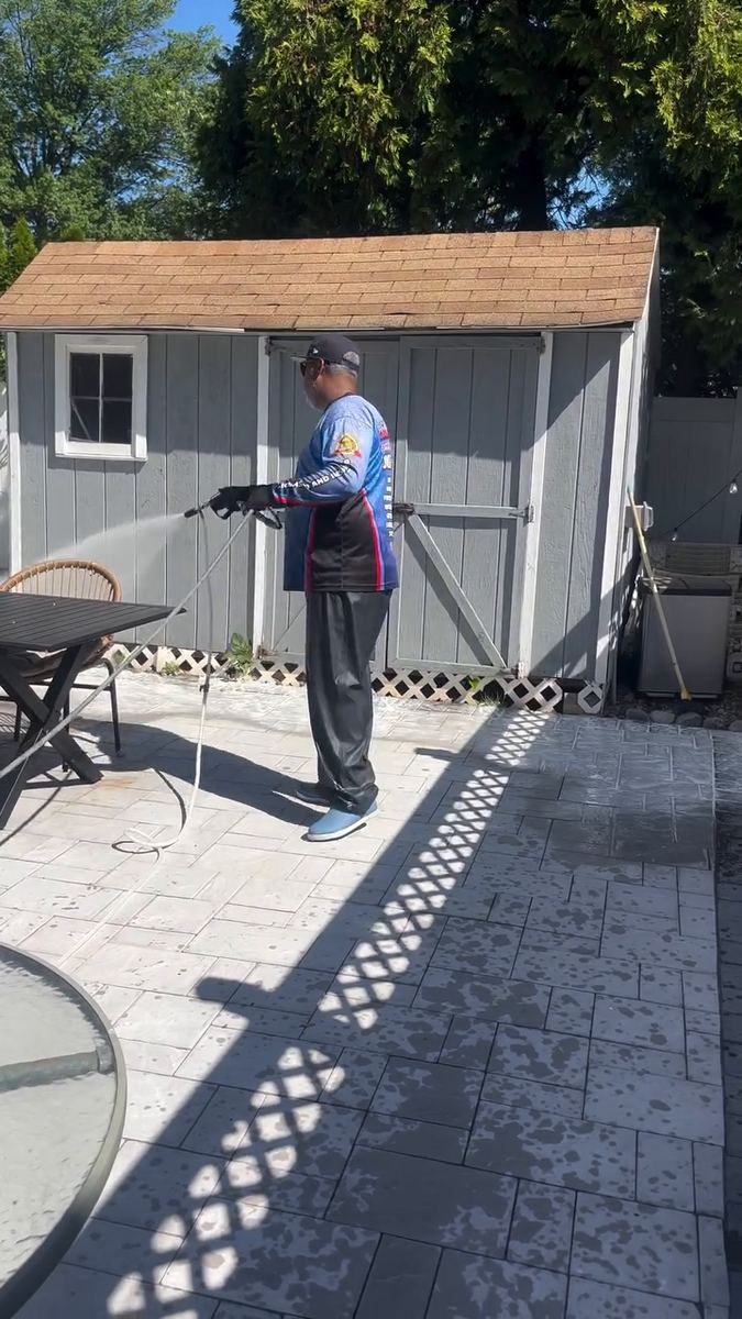 A Premier Power Washerz technician washing a paver patio in front of a backyard shed