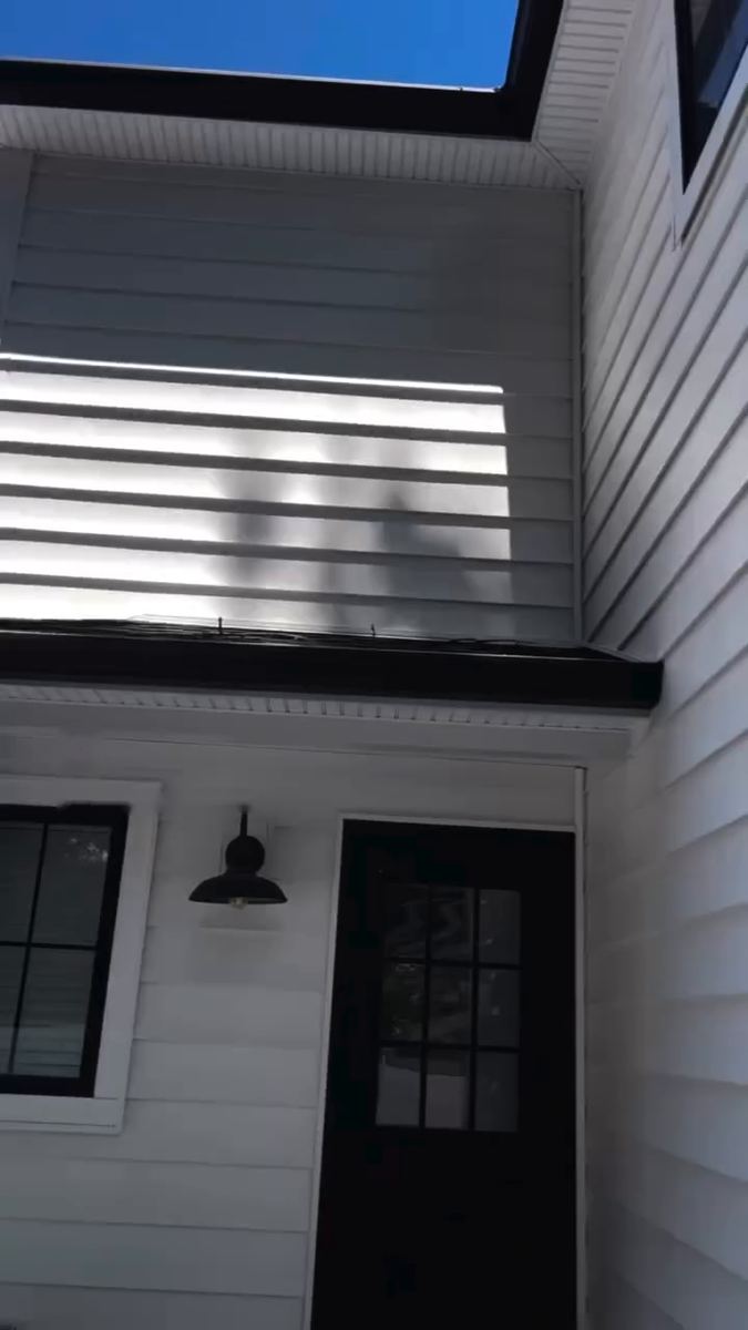 Bright white vinyl siding above a black framed door and windows after cleaning