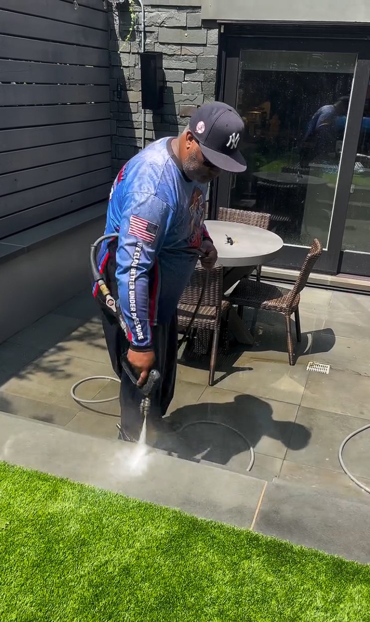 A technician surface cleaning the bluestone patio beside artificial turf and a dining set