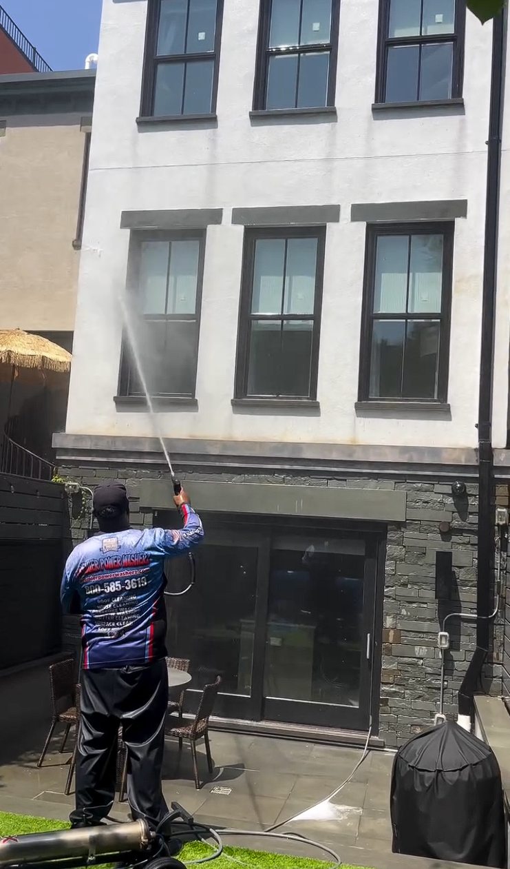 A technician soft washing the white stucco rear elevation of the brownstone above a stone clad ground floor and patio