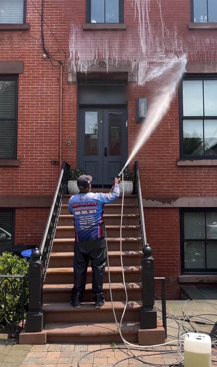 A Premier Power Washerz technician soft washing the brick facade of a Hoboken brownstone from the stoop