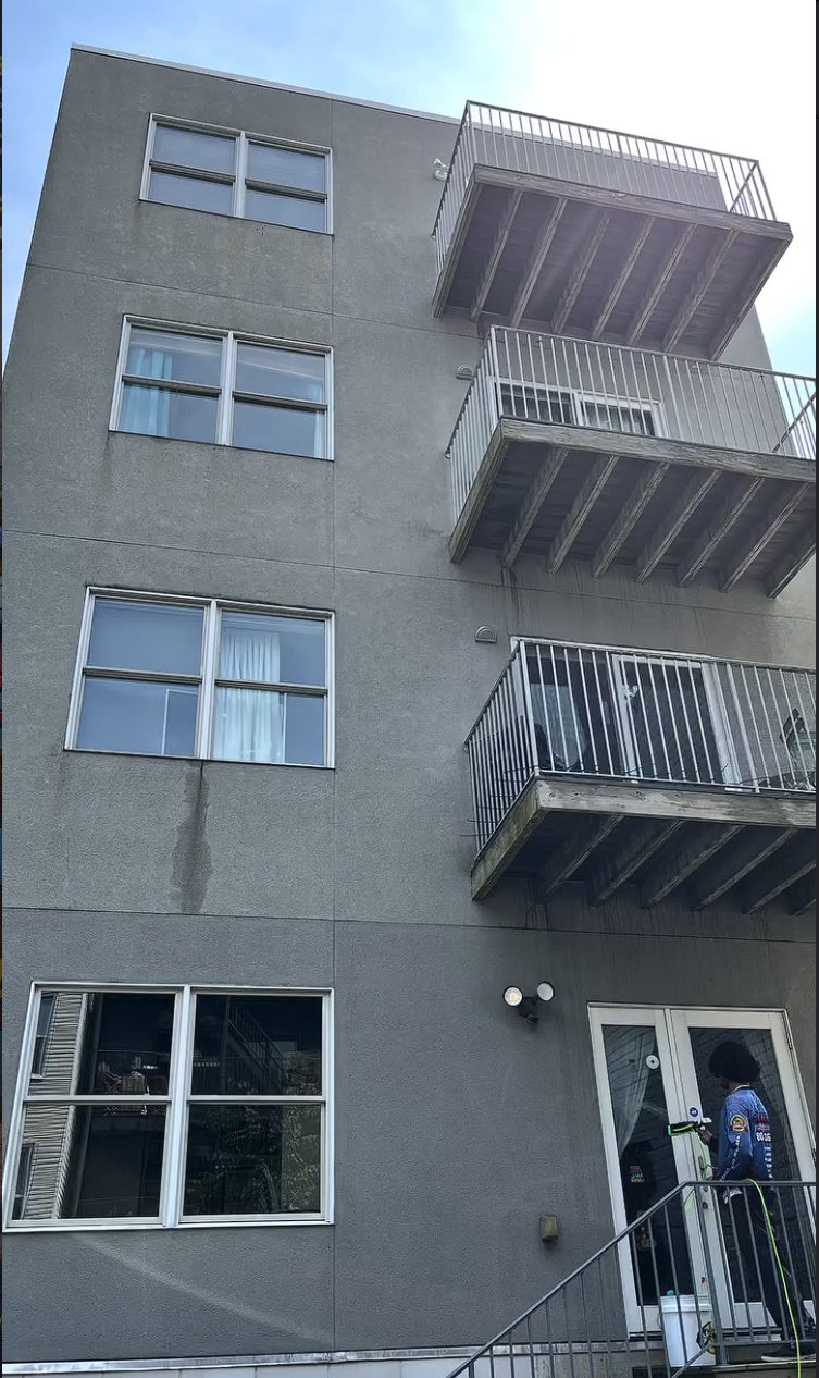 The full rear stucco elevation of the building with a technician working at the ground floor doors