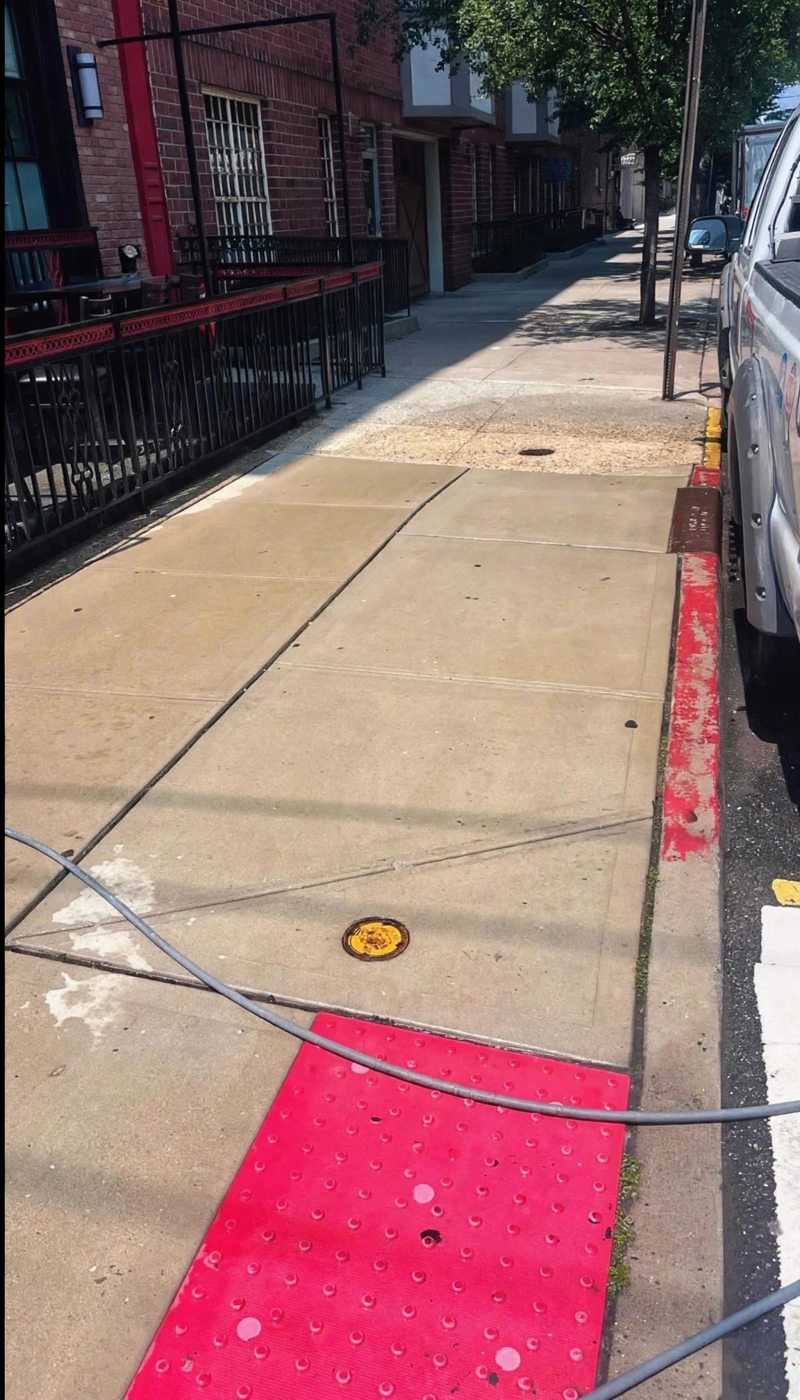 A Hoboken restaurant sidewalk mid cleaning with a clear line between washed and grimy concrete