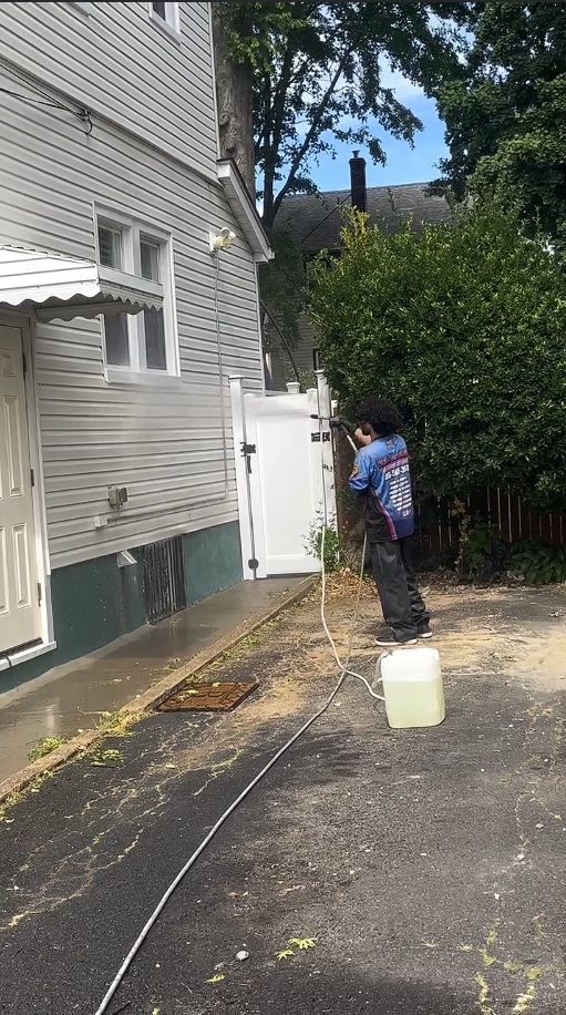 A technician treating the awning side of the house beside tall hedges