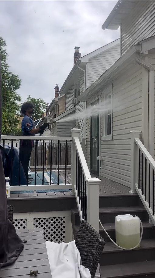 A technician washing the upper siding from the pool deck at the rear of the house