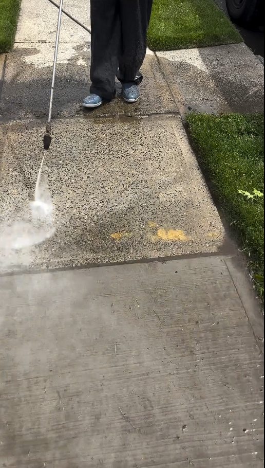 A concrete walkway mid cleaning with a visible line between the washed and unwashed sections