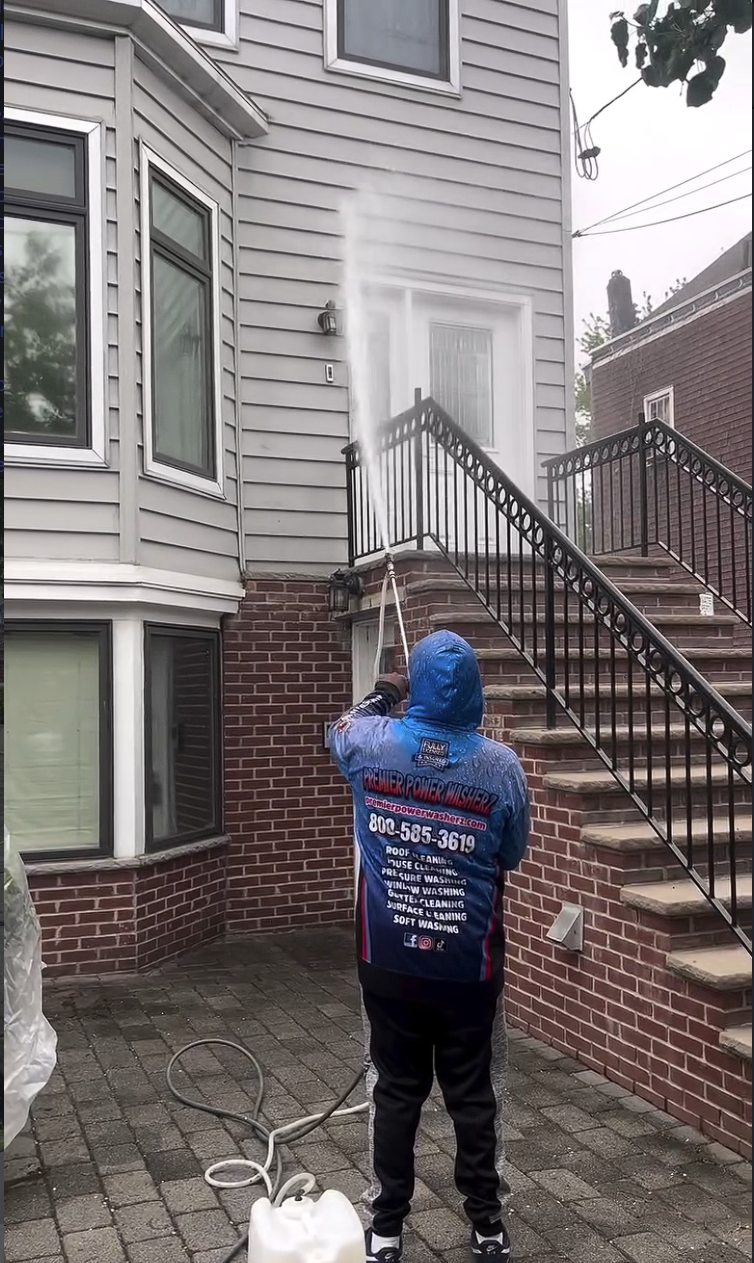 A Premier Power Washerz crew member soft washing the front facade of the home