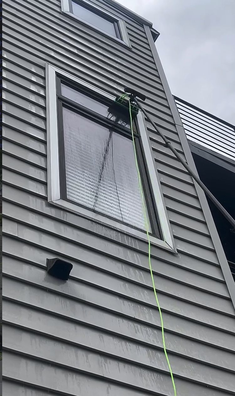 A water fed pole brush cleaning an upper floor window on the gray sided home