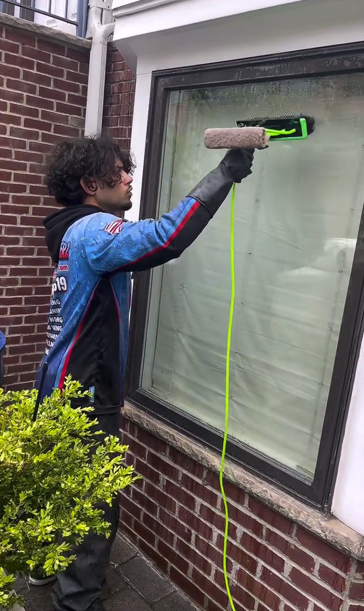 A crew member hand squeegeeing a ground floor window beside brick