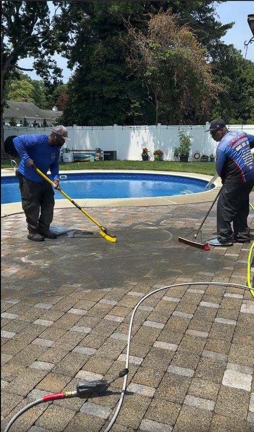 Two crew members spreading and working joint sand across the pool deck pavers