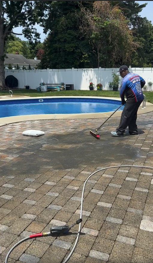 A Premier Power Washerz technician sweeping fresh sand into paver joints beside the pool